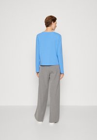 Top azzurro chiaro a maniche lunghe con scollatura rotonda, abbinato a pantaloni grigi a gamba larga, caratterizzati da una texture liscia e una vestibilità comoda.