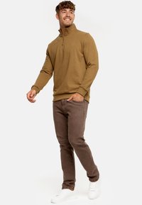 Brun zip-up sweatshirt med høj krave, ribbede manchetter og en afslappet pasform, parret med brune slim-fit bukser og hvide sneakers.
