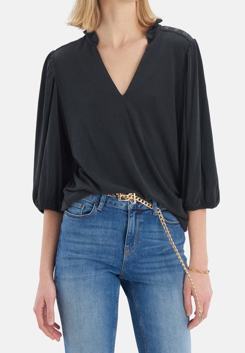 Blouse noire à coupe ample avec un décolleté en V profond, manches bouffantes et détails à boutons sur les épaules, fabriquée en tissu doux et respirant.