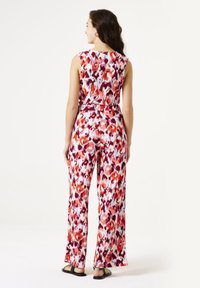 Achteraanzicht van een mouwloze jumpsuit in een levendig bloemenpatroon met oranje, roze en paarse tinten, met een ontspannen pasvorm en wijde benen.