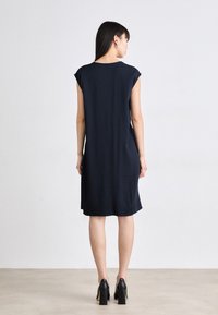 Navy short-sleeve dress with a relaxed fit, knee-length, and soft fabric. Worn with black high-heeled shoes, displaying a simple design.