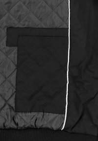 Tissu matelassé noir avec deux patchs rectangulaires noirs superposés et une bordure verticale blanche sur un tissu noir lisse.