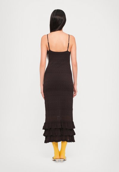 Bruine, gebreide maxi-jurk met dunne bandjes, met een gerimpelde zoom en ribbelstructuur. Gecombineerd met gele sokken en(open) schoenen.