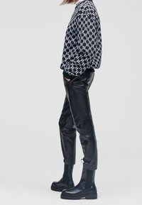 Schwarz-weiß gemustertes Sweatshirt, Ledershosen und schwarze Stiefeletten mit klobigen Sohlen. Das Design zeigt ein markantes Blitzmotiv.