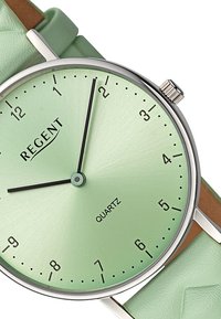 Montre à quartz avec un cadran vert menthe brossé, une lunette en argent, des index horaires noirs et un bracelet en cuir vert menthe avec une finition texturée.