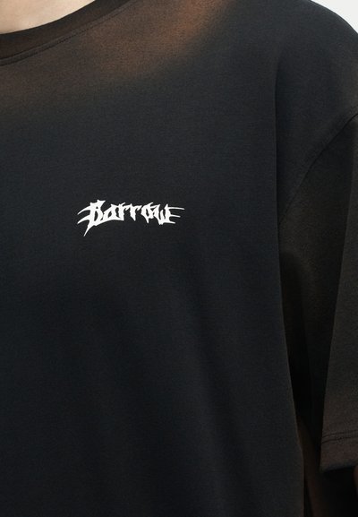 Μαύρο T-shirt με λευκό, στυλιζαρισμένο κείμενο "Barrow" στο κέντρο του πάνω μέρους του στήθους, που φοριέται από ένα άτομο με ουδέτερο φόντο.