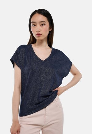 T-shirt bleu marine à col V avec des manches courtes, fabriqué à partir d'un matériau pailleté. Présente une coupe décontractée et une texture lisse. Associé à un pantalon de couleur claire.