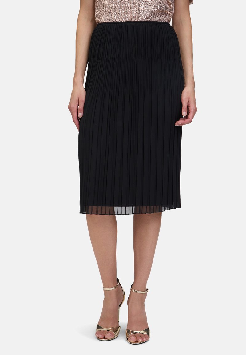 Zwarte geplooide rok met een lengte tot halverwege de kuit en een doorschijnende zoom. Gecombineerd met gouden open teenhakken. Opvallende textuur voegt visuele interesse toe.