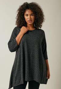 Schwarzes Tunika-Oberteil mit dreiviertellangen Ärmeln, das aus einem strukturierten Gewebe mit kleinen silbernen Punkten besteht, runder Ausschnitt und einer lockeren Silhouette.