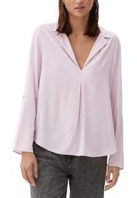 Blusa rosa chiaro con maniche lunghe, scollatura a V profonda e vestibilità ampia. Texture liscia e dettaglio piegato al centro. Abbinata a jeans grigi scuri.