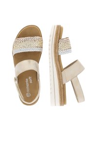 Sandales beige clair avec des brides métalliques tissées, semelle rembourrée, sangle de cheville ajustable et semelle texturée.