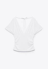 Blouse blanche à manches courtes avec un profond col en V, taille froncée et fermeture nouée au dos.