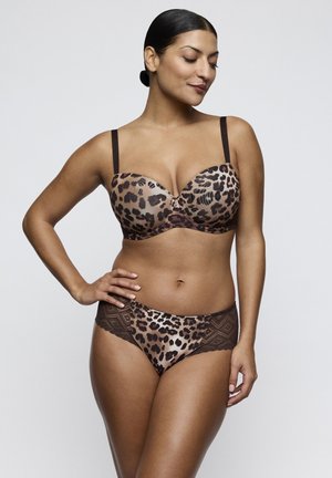 Woman with dark hair in a leopard print bra with thin straps and matching panties with lace sides, posing with one hand on hip against a plain background.
