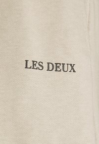 Tissu en coton beige avec une texture côtelée, arborant le nom imprimé "LES DEUX" en noir. Design simple sans motifs ni accents supplémentaires.