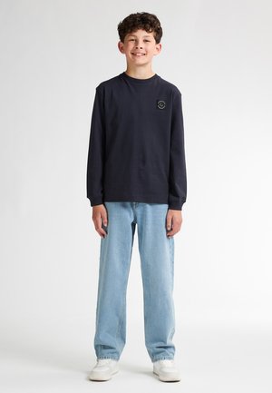 T-shirt à manches longues bleu marine avec un petit logo blanc, jean droit bleu clair et baskets blanches. Design minimaliste et coupe décontractée.