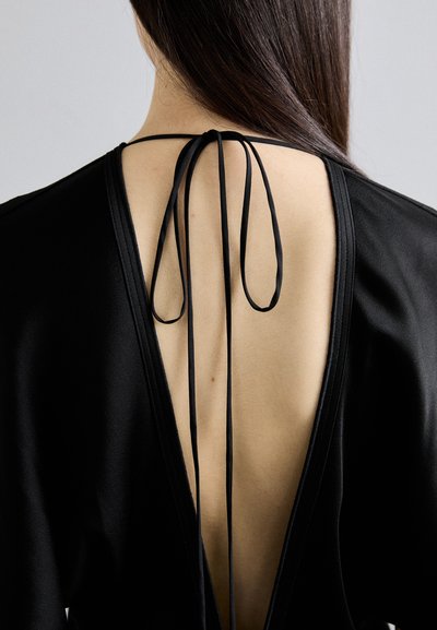 Zwarte kledingstuk met een diepe V-rug en dunne strikbandjes. De gladde, matte textuur versterkt het minimalistische ontwerp.