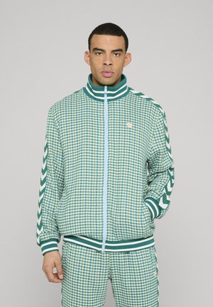 Grøn og hvid hundetandsmønstret lynlåstrøje med stribet krave og ærmekanter, kombineret med matchende bukser; indeholder en diskret logo på brystet.