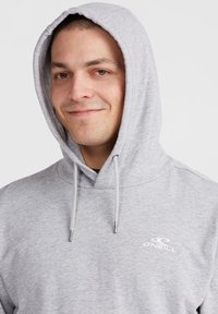 Hoodie gris avec capuche à cordon, texture douce et petit logo blanc sur la poitrine. Design simple, coupe décontractée.
