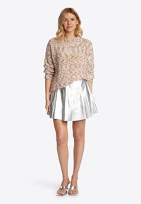 Rosa Strickpullover mit floralen Sprenkeln, kombiniert mit einem metallisch silbernen Faltenrock. Das Model trägt silberne Sandalen; die glatte Textur ist deutlich zu erkennen.