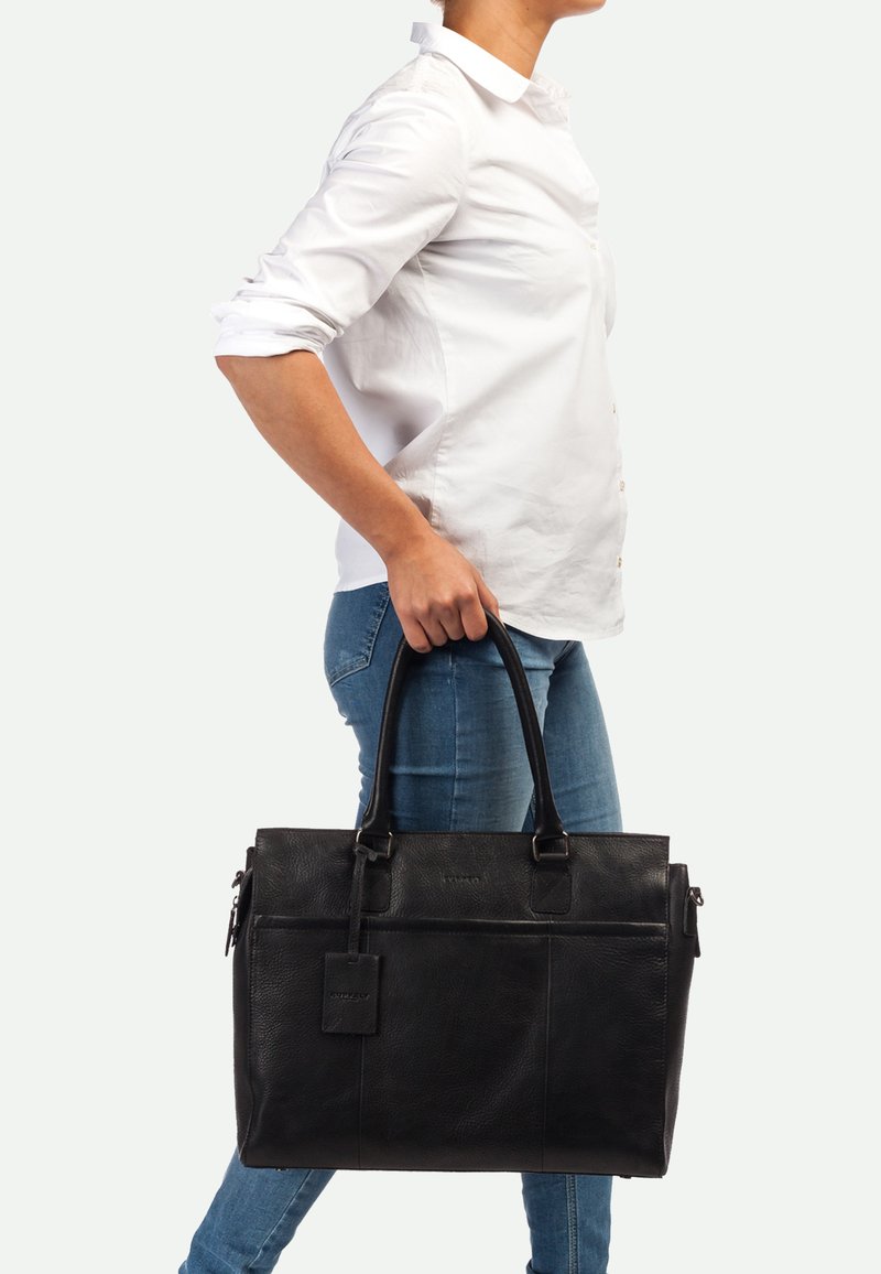 Bolso tote de cuero negro con dos asas, cierre con cremallera, compartimento frontal y una etiqueta desmontable. Textura suave con un sutil detalle de grano.