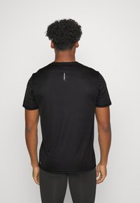 Mustat urheilupaidat, joissa on lyhyet hihat, pyöreä kaula-aukko ja minimalistinen valkoinen logo takana. Sujuva, kevyt kangas.