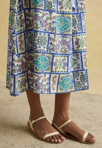 Mehrfarbige gemusterte Sommerkleid mit floralen und geometrischen Designs; beige flache Sandalen mit dünnen Riemen und verstellbarem Knöchelverschluss.