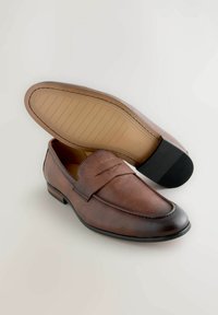 Braune Lederloafers mit einem erhöhten Nahtdetail. Glatte Textur an der Zehenpartie und eine kontrastierende Gummisohle mit linearer Profiltiefe.