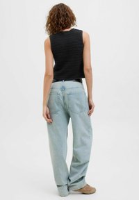 Mustmustritsiga must tank top, millel on seljaosal taskud ja mugav lõige, kombineeritud helesiniste suurte teksadega, lõpetatud beežide jalatsitega.