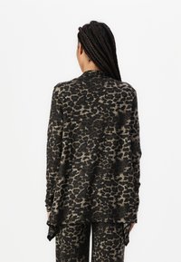 Långärmad topp i leopardmönster, med ett mjukt tyg, avslappnad passform och en rundad nederkant bak. Främst svart och beige.
