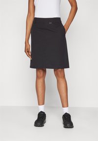 Falda negra de corte ajustado, con tejido ligero, textura suave y bolsillos laterales. Llevada con una blusa blanca ceñida y zapatos negros.