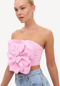 Jeune femme portant un crop top rose sans bretelles avec un grand détail de fleur en tissu et un jean taille haute bleu clair.