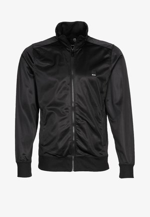 Černá bunda na zip vyrobená z hladké, lehké tkaniny. Má stojací límec a žebrované manžety s malým logem na hrudi.