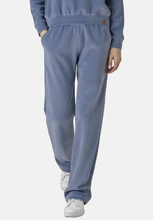 Blaue Fleece-Jogginghosen mit elastischem Bund und Seitentaschen. Sie verfügen über eine weiche Textur und eine lockere Passform, kombiniert mit weißen Sneakers.