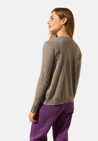 Pull en tricot gris avec un col rond, des manches longues et des boutons décoratifs aux poignets, associé à un pantalon violet.