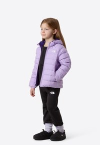 Ανοιχτό μωβ μπουφάν puffer με κουκούλα, με φερμουάρ και το λογότυπο The North Face, συνδυασμένο με μαύρο παντελόνι και μαύρα παπούτσια τύπου slip-on.