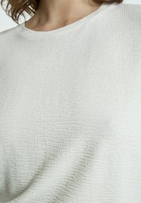 Top de crema claro texturizado con escote redondo; presenta un sutil patrón geométrico y una tela suave y tejida para mayor comodidad.