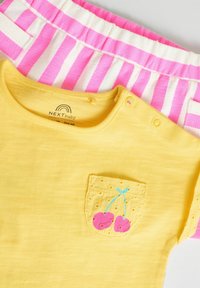 T-shirt en coton jaune avec une poche ornée de cerises brodées, associée à un short rayé rose et blanc avec une taille élastique.
