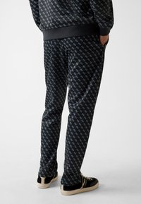 Schwarze Jogginghosen mit Diamantmuster, ausgestattet mit einem Bund, Seitentaschen und kombiniert mit schwarzen Sneakers. Weicher, strukturierter Stoff.