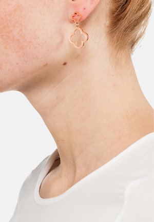 Ohrringe in Roségold in Form einer Blume mit ausgeschnittenem Design. Die Ohrringe hängen an einem kleinen Stecker und verfügen über glatte Oberflächen sowie eine zarte Textur.
