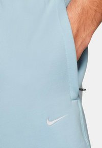 Pantalones cortos Nike de color azul claro, fabricados con una tela suave, que cuentan con un bolsillo lateral y un pequeño logo blanco cerca del dobladillo. Textura suave, diseño casual.