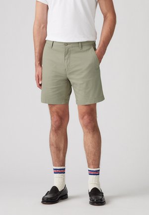 Pantaloni corti verdi fino al ginocchio realizzati in tessuto leggero, con una parte anteriore piatta e tasche laterali, abbinati a calze bianche e mocassini neri.