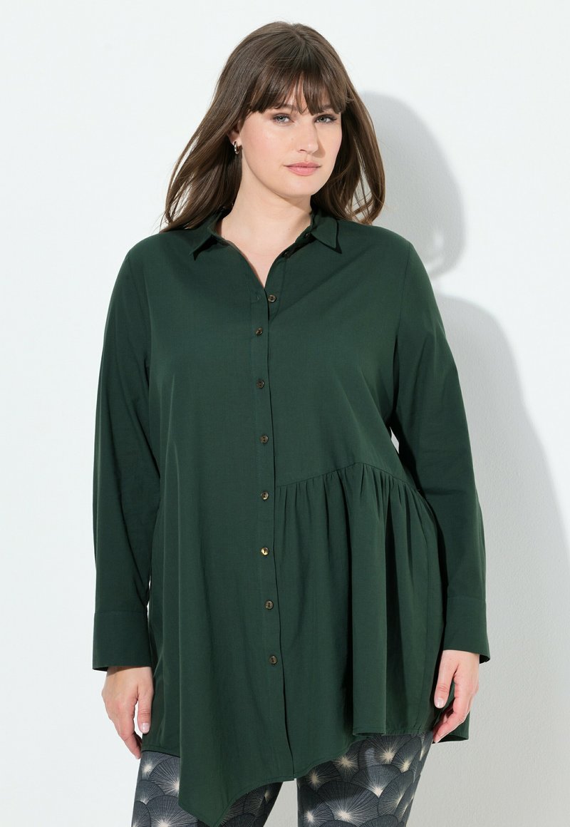 Camicia button-up verde scuro con orlo plissettato, maniche lunghe e colletto; presenta bottoni dorati e una vestibilità leggermente ampia.