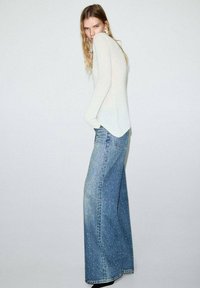 Suéter claro, ligero y de manga larga combinado con unos vaqueros de talle alto y pierna ancha que presentan un patrón salpicado y una textura sutil.