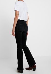 Jeans acampanados negros de talle medio, con una textura suave y bolsillos traseros. Combinados con una camiseta blanca y botas de tacón marrones.