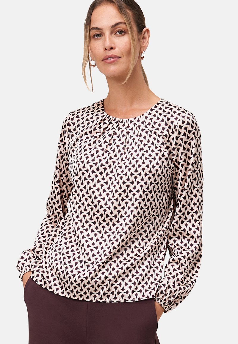 Fließende Bluse in Hellrosa mit geometrischem Muster in Dunkelmaroon. Verfügt über lange Ärmel und einen gerafften Ausschnitt. Weiche Stoffstruktur.