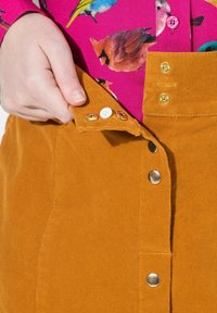 Corduroy-Rock in Senfgelb mit knöpfbarem Vorderteil, ausgestattet mit goldfarbenen Beschlägen und einer strukturierten gerippten Oberfläche.