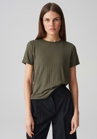 Olive green ribbed t-shirt with a round neckline and short sleeves, paired with black pants. Smooth texture with a fitted design.