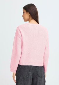 Pulover roz cu dungi, cu gât rotund, umeri căzuți și mâneci lungi. Cureaua este ușor scurtată, creând o croială lejeră.