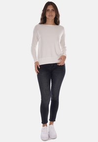 Maglietta bianca a maniche lunghe in tessuto leggero, abbinata a jeans skinny scuri e sneakers bianche. Tessuto liscio, vestibilità comoda e orlo a coste.