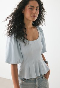 Helles blaues Oberteil mit kurzen Ärmeln, quadratischem Ausschnitt und puffigen Ärmeln, mit vertikalen Nähten und einem ausgestellten Saum, kombiniert mit zerstörten Jeans.